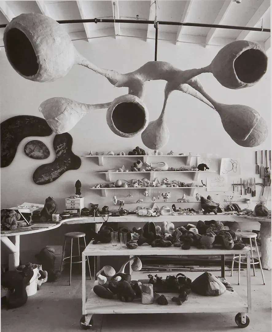 Studio workspace with suspended sculptural vessel installation overhead and shelving displaying ceramic pieces and objects by Rogan Gregory.