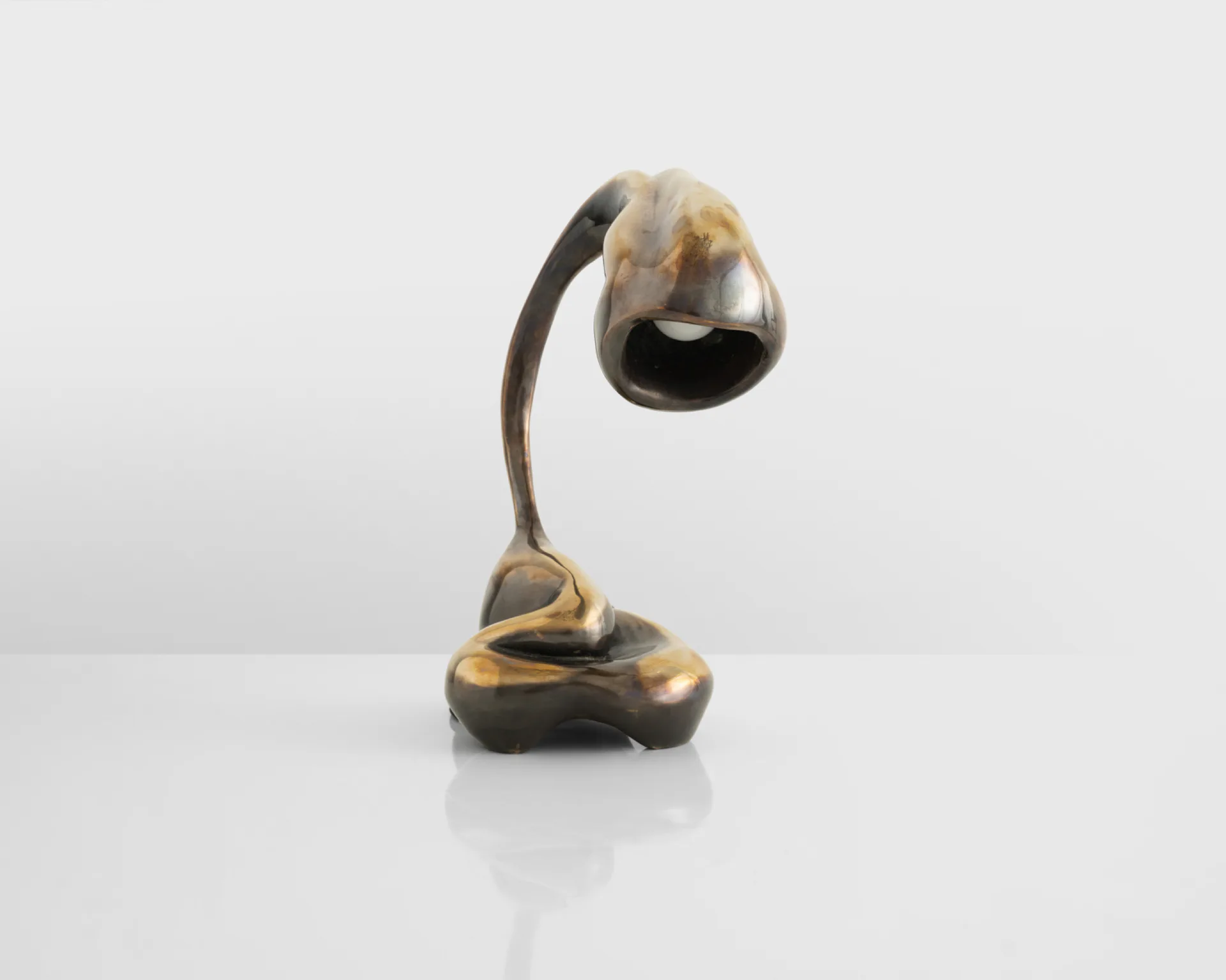 Bronze sculptural desk lamp with curved arch and organic base, featuring gold and dark patina finishes, by Rogan Gregory.