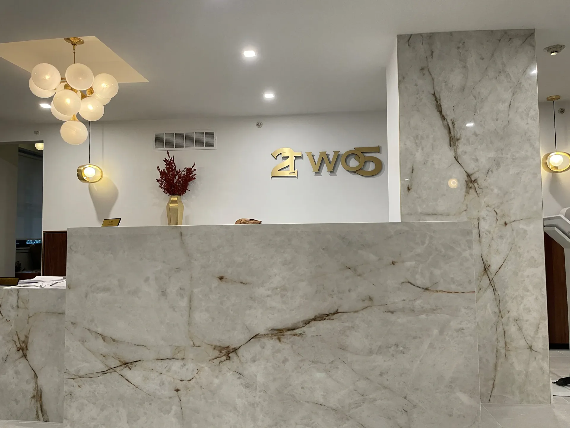 Modern reception desk with marble cladding, brass signage, sculptural pendant lighting, and minimalist aesthetic by Rosanna Trivilino.