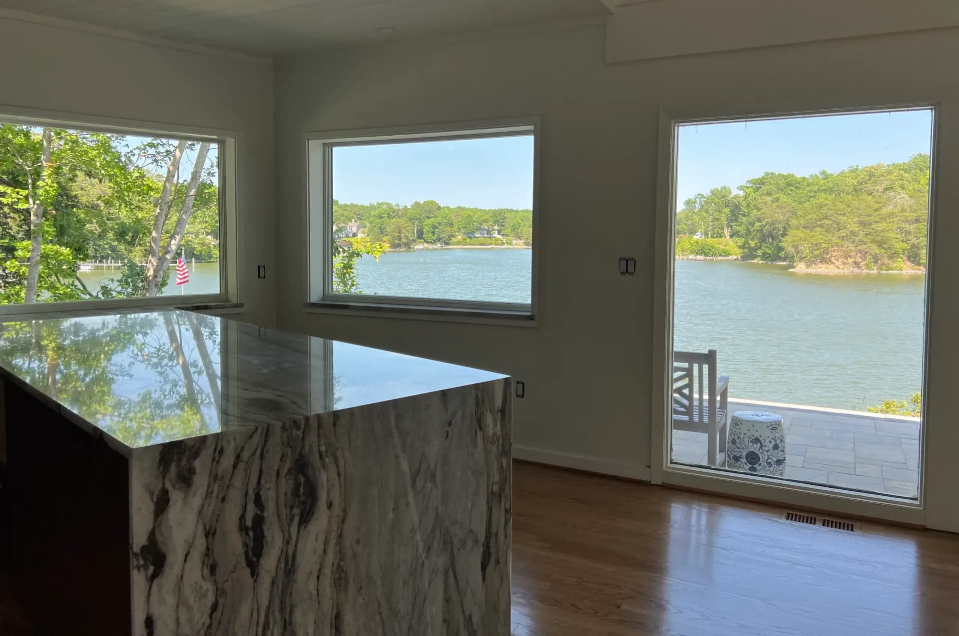 Modern lakeside interior with marble kitchen island, wide windows framing water views, and natural wood flooring by Rosanna Trivilino.