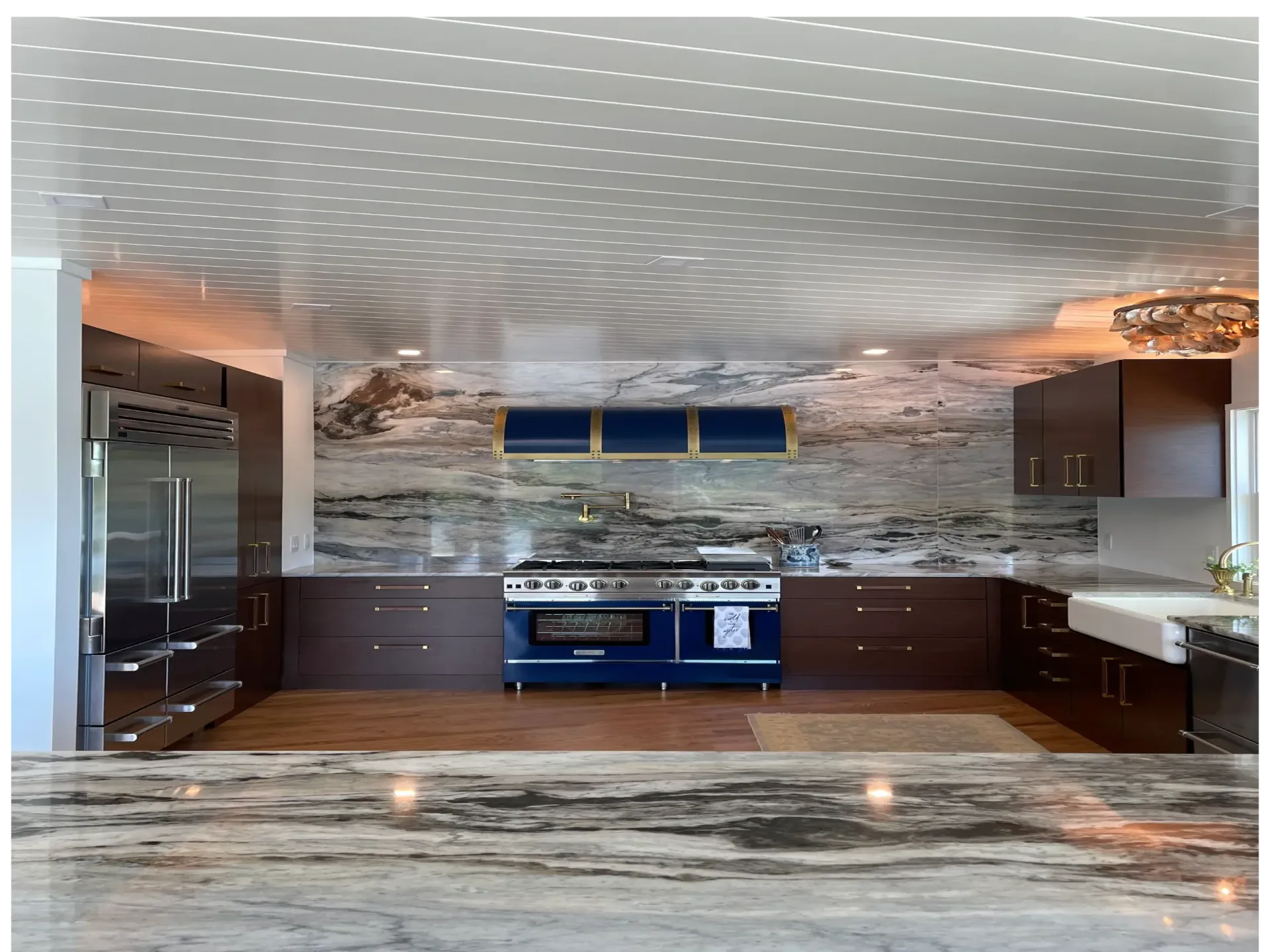 Modern kitchen with dark cabinetry, blue Lacanche range, marble backsplash and countertops, stainless steel appliances, and blue upper cabinets by Rosanna Trivilino.