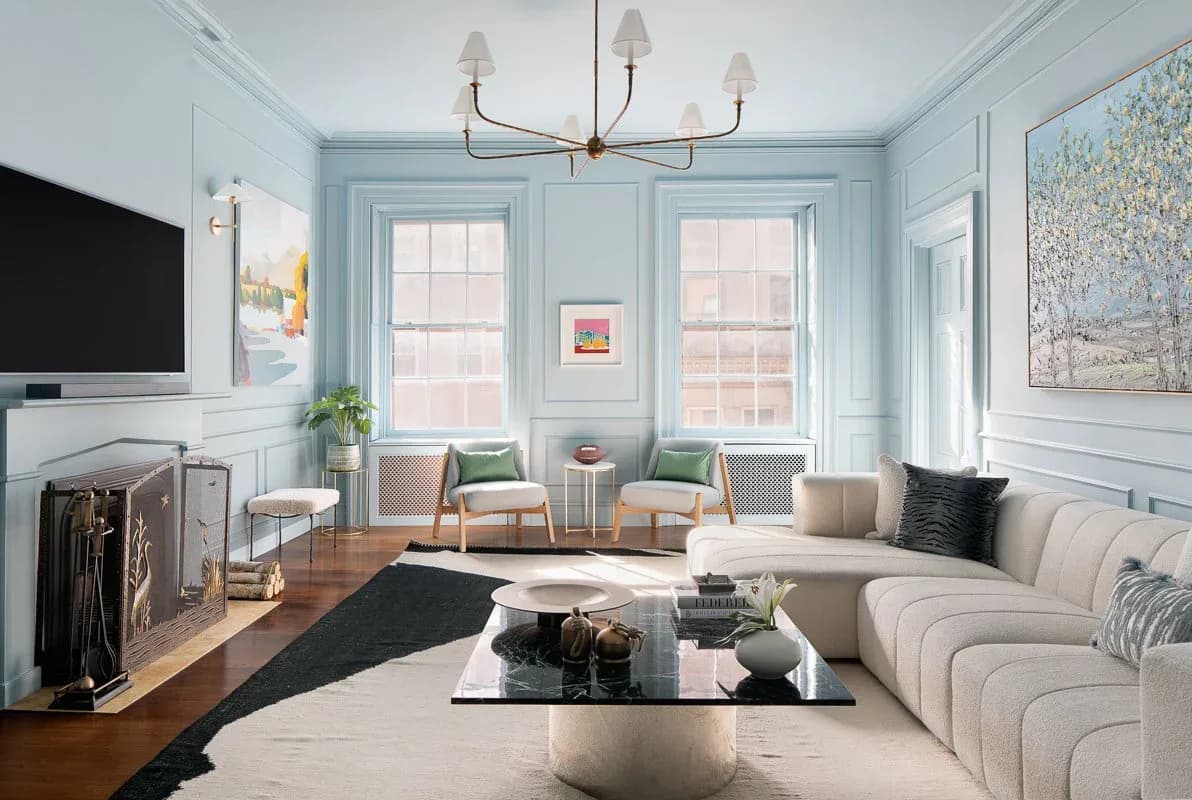 Light blue living room with curved cream sectional, large windows, brass chandelier, and contemporary furnishings designed by Ruchi Mohan.