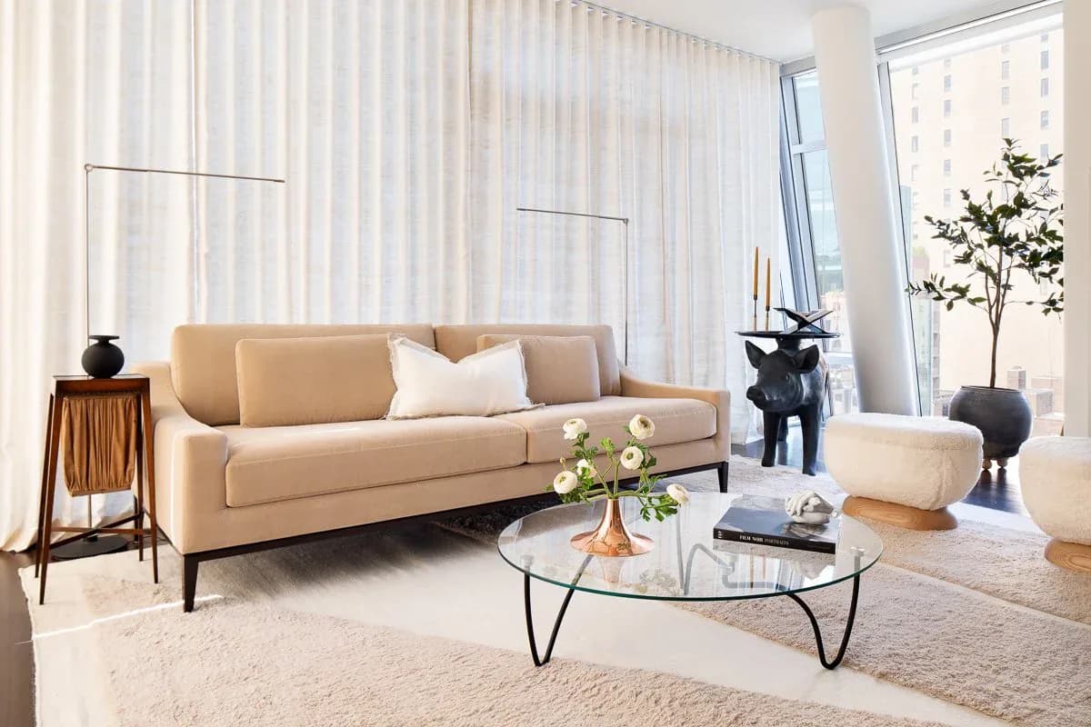 Modern living room with caramel-toned sofa, glass coffee table, and floor-to-ceiling sheer curtains in a minimalist aesthetic by Ruchi Mohan.