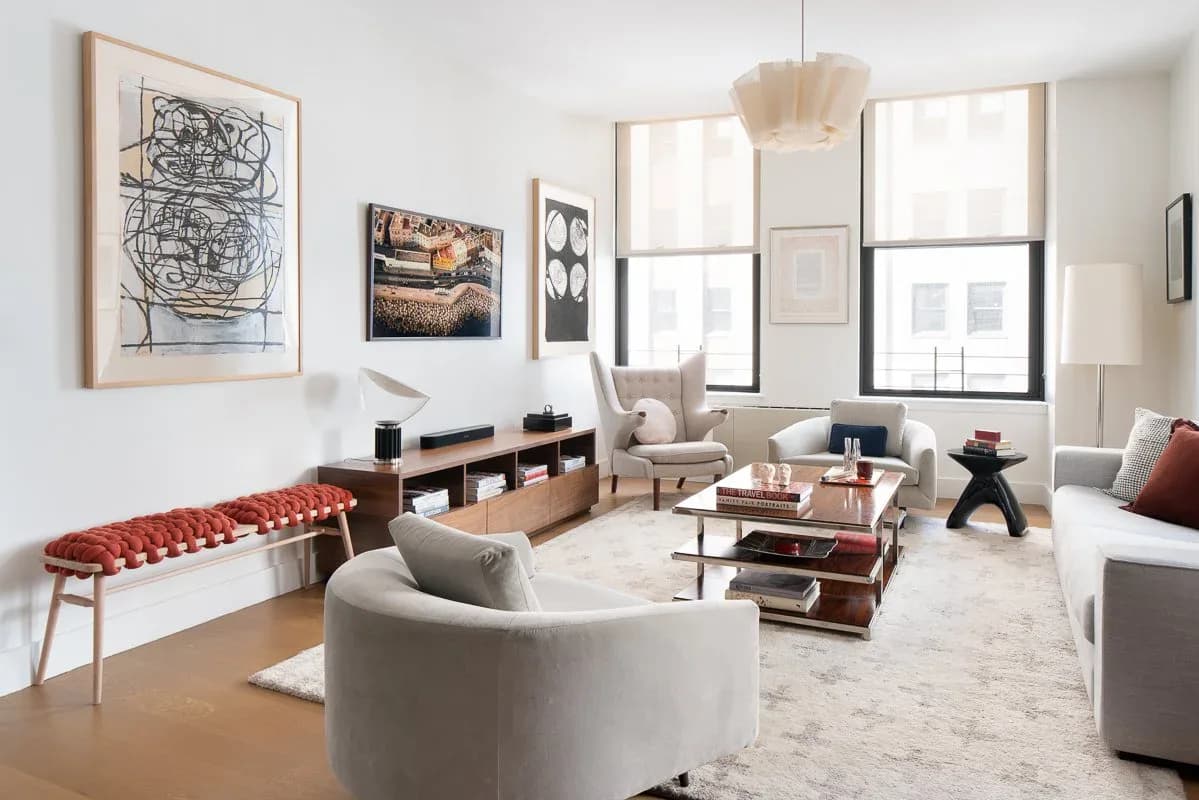 Modern living room with curved cream sofa, wooden storage, red tufted bench, and large windows, designed by Ruchi Mohan.