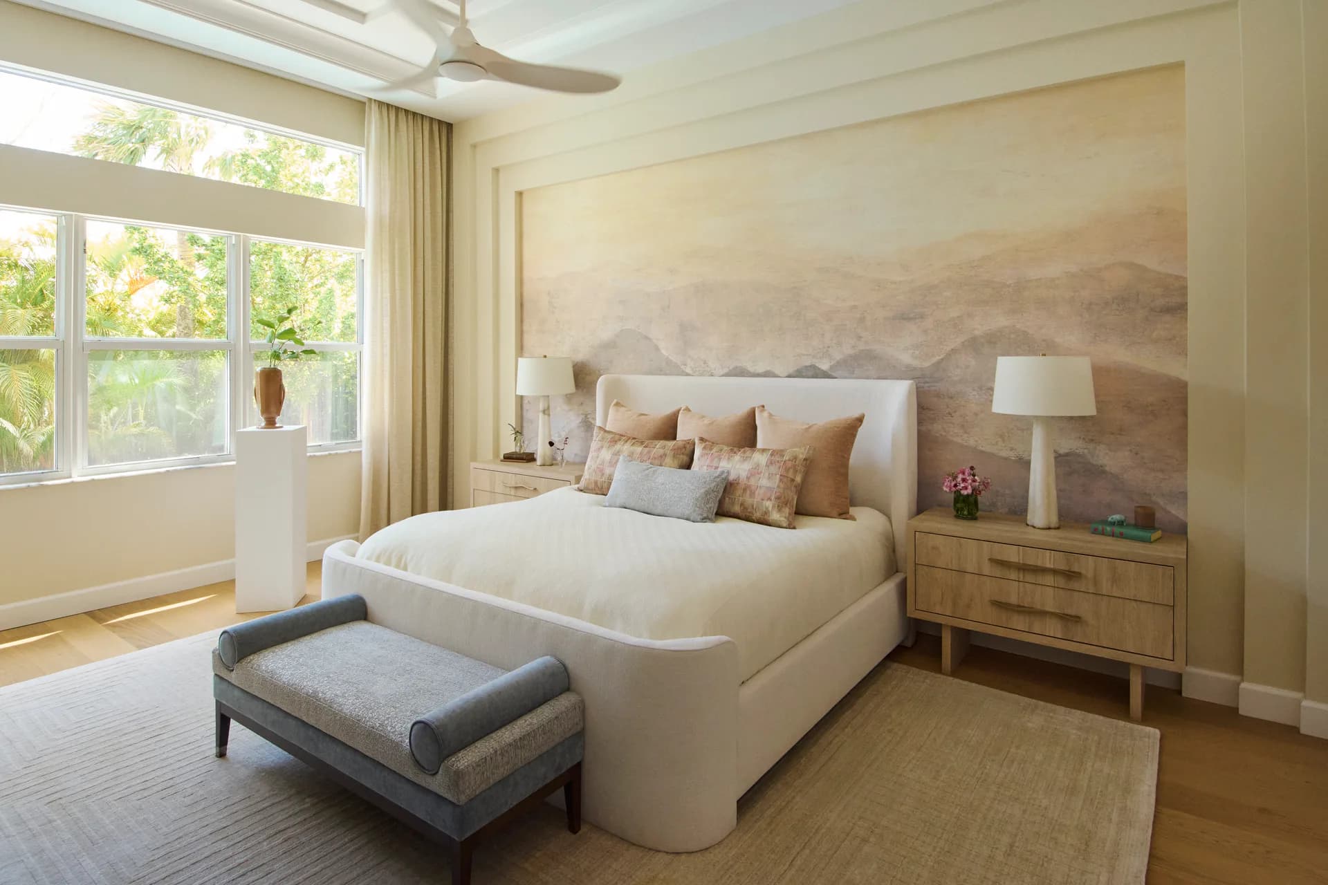 Modern bedroom with curved white bed, wooden nightstands, and large abstract landscape artwork above headboard, designed by Russell Goldman.