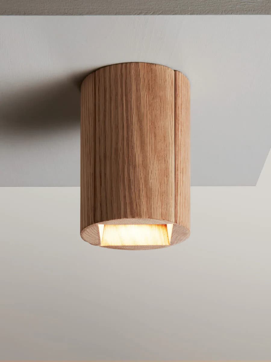 Cylindrical wooden ceiling-mounted light fixture with vertical grain detailing and warm interior glow by Russell Greenberg.