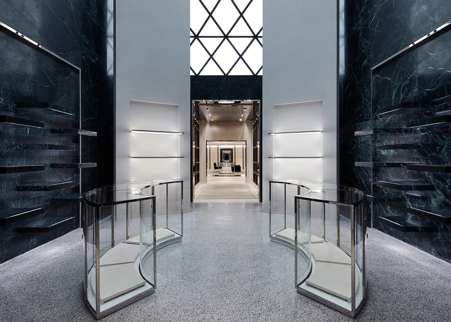 Symmetrical luxury retail corridor with black marble walls, polished concrete flooring, and geometric skylight, designed by Ryan Korban.