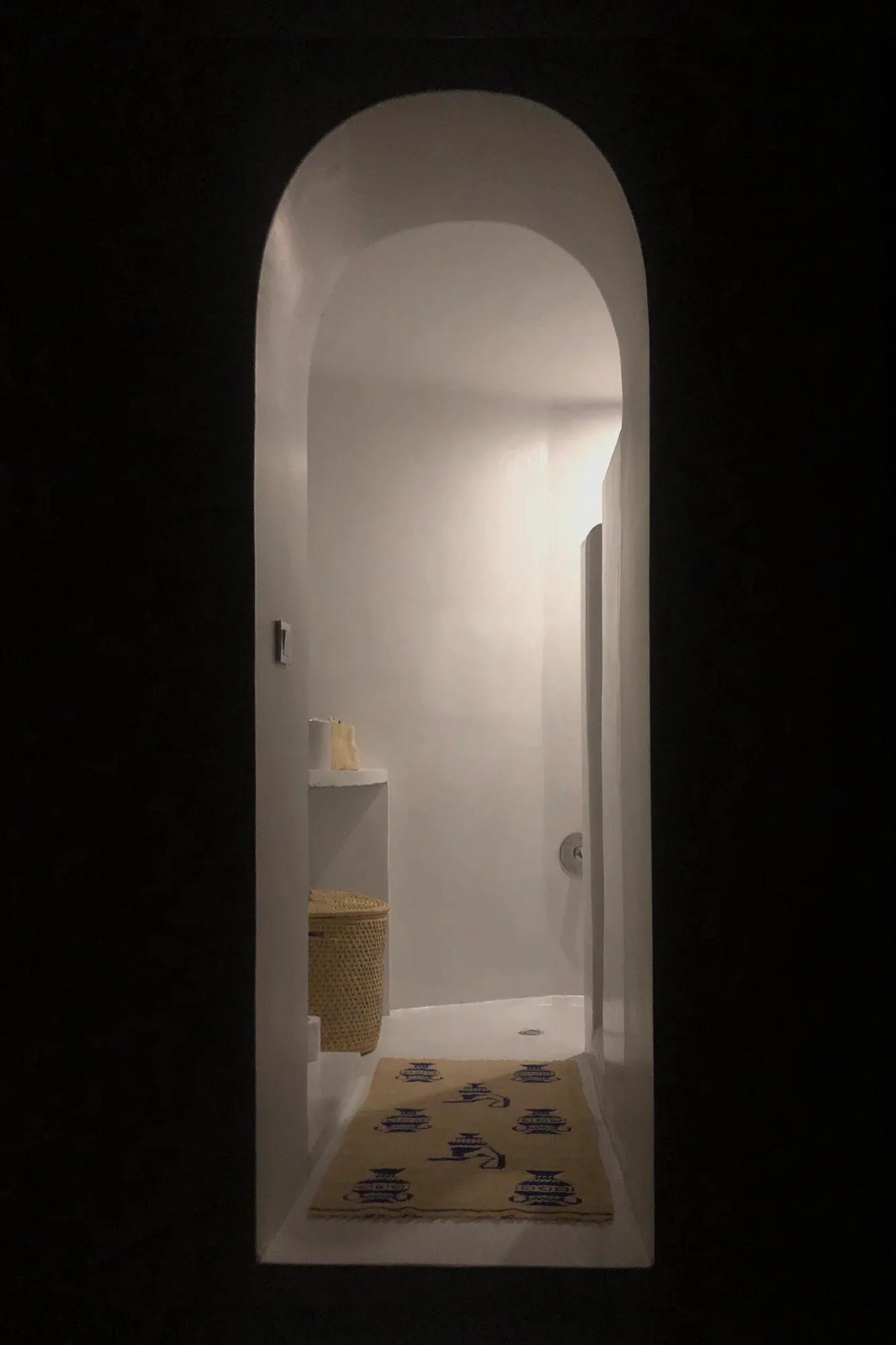 Minimalist white arched corridor with natural lighting, woven basket accent, and patterned floor mat by Saba Yazdjerdi.