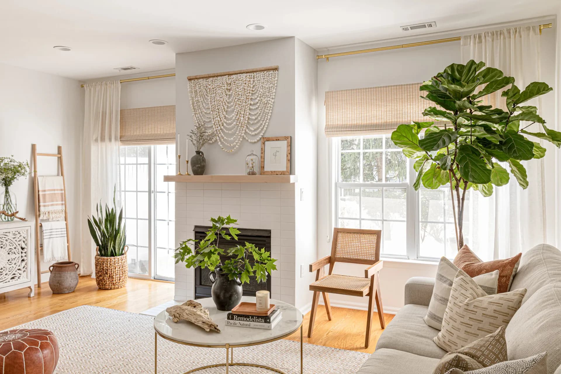 Bright living room with neutral palette, fireplace with built-in shelving, large windows, abundant plants, and mid-century modern furniture by Sabrina Vroeg.