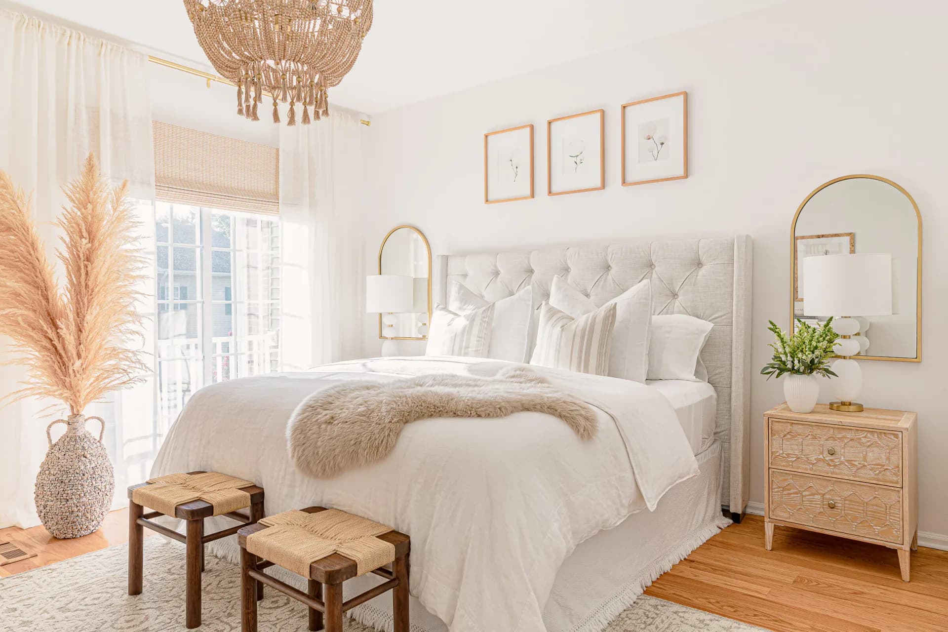 Serene bedroom with neutral palette featuring a beige upholstered headboard, white bedding, natural wood furniture, woven pendant light, and gold-framed mirror by Sabrina Vroeg.
