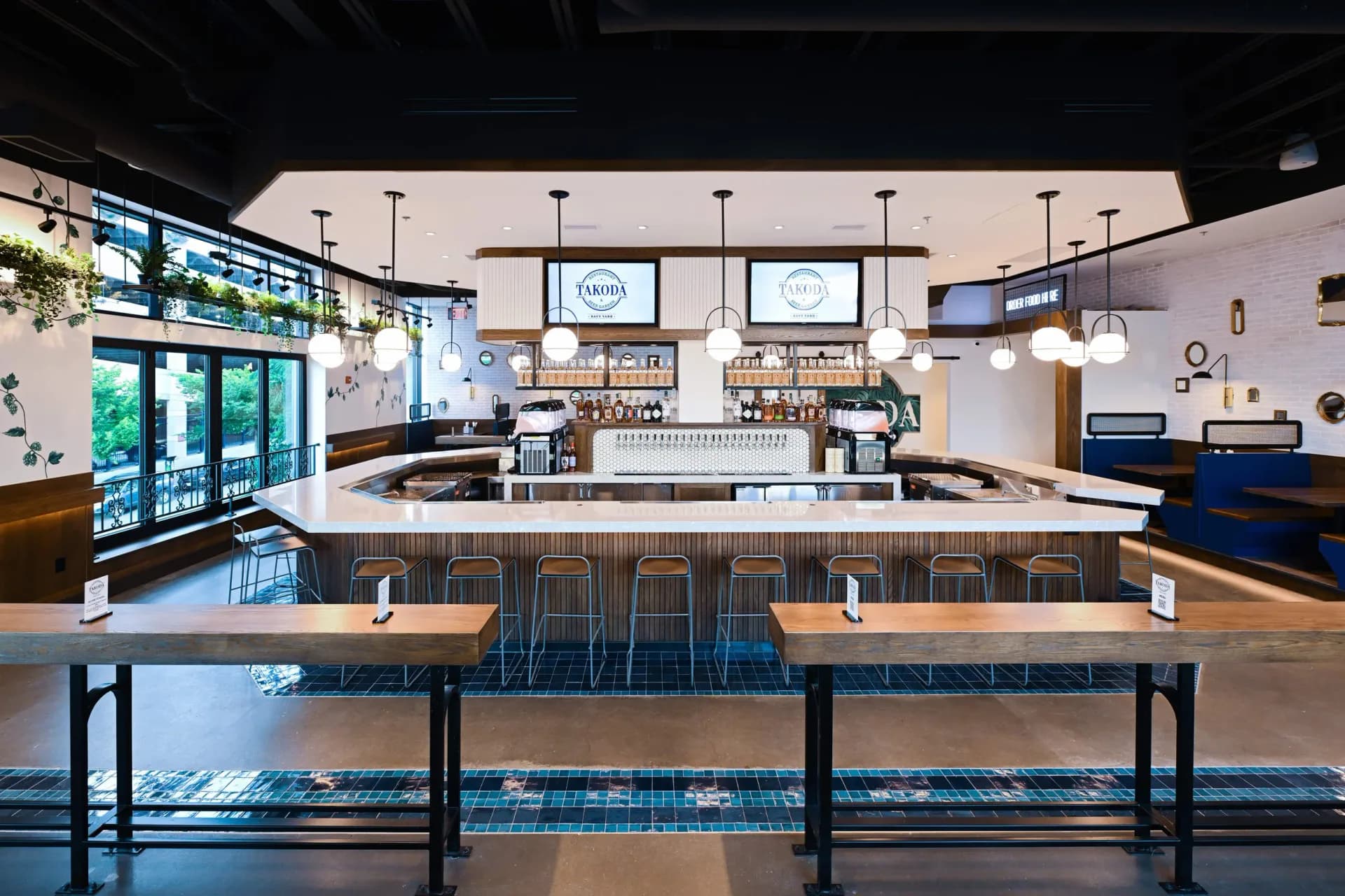 Modern brewery or taproom interior with central bar counter, wooden tables, pendant lighting, and blue accent flooring, designed by Sam Forman.