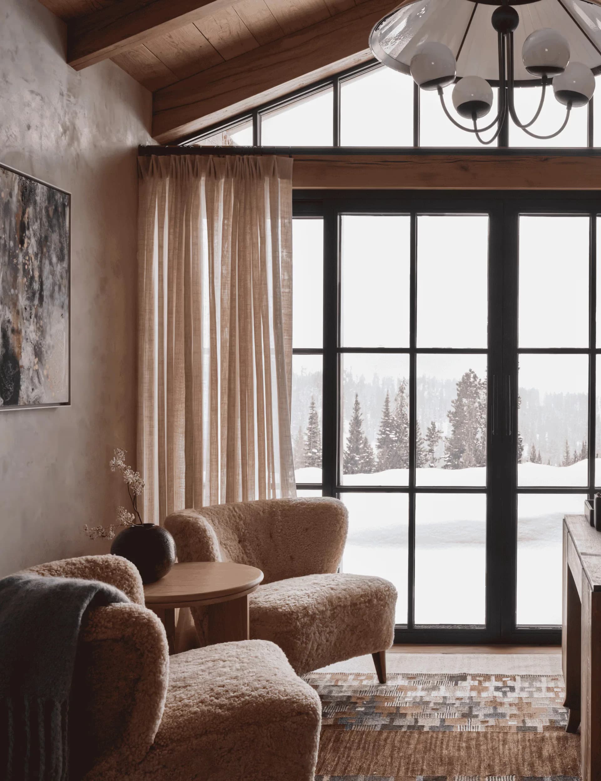 Modern mountain lodge interior with curved caramel upholstered seating, floor-to-ceiling black-framed doors, neutral linen curtains, and snowy forest views by Samantha Hemsworth.