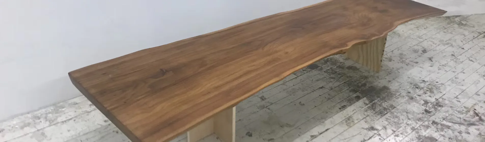 Walnut live-edge dining table with curved top and light wood base on polished concrete floor by Sandy Smith.