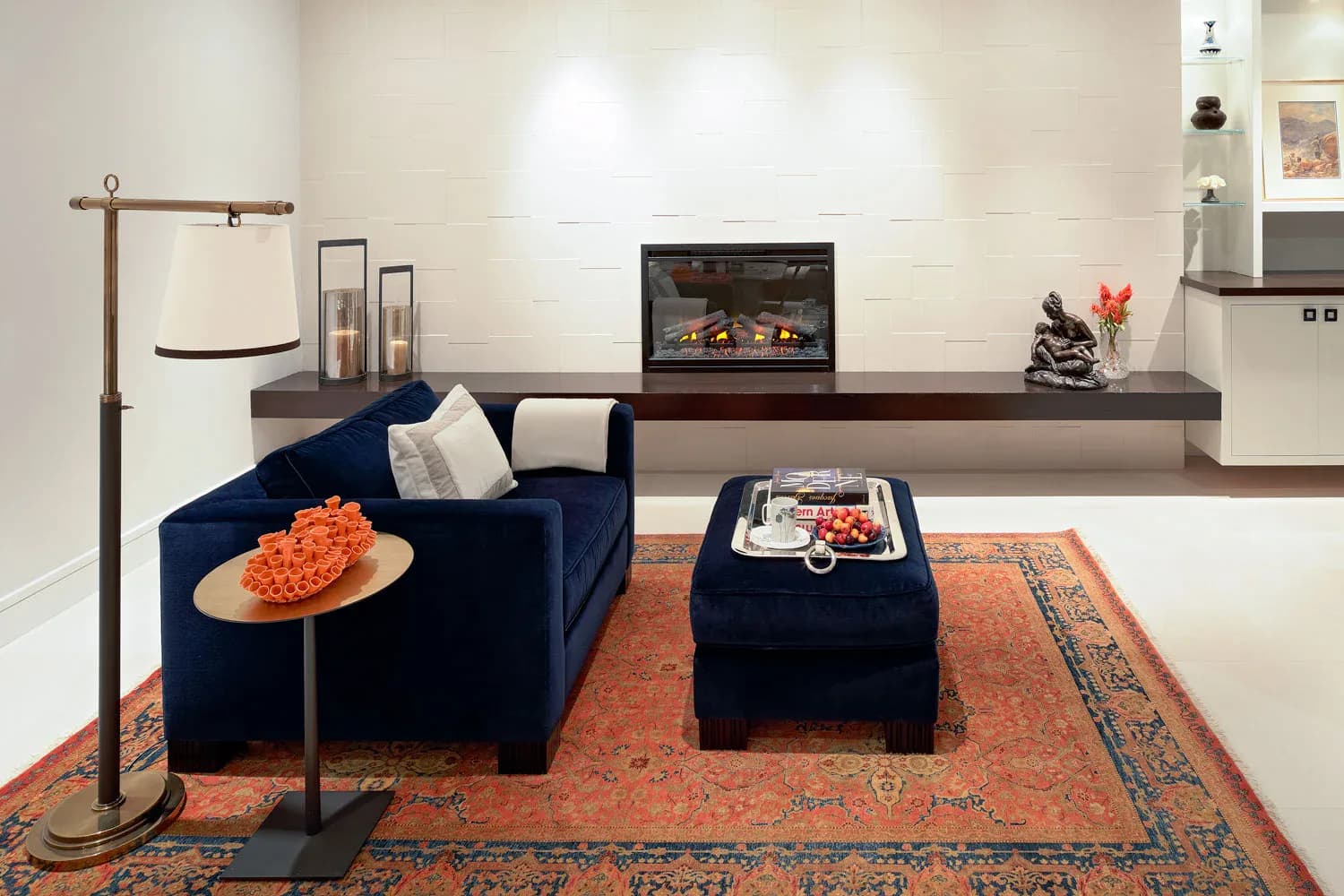 Modern living room with navy velvet curved sofa, orange patterned rug, fireplace, and minimalist décor by Sara Jazayeri.
