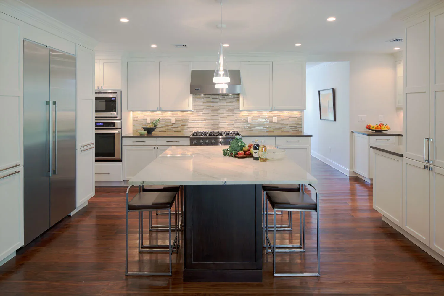 Modern kitchen with white cabinetry, dark waterfall island, stainless steel appliances, and warm wood flooring by Sara Jazayeri.
