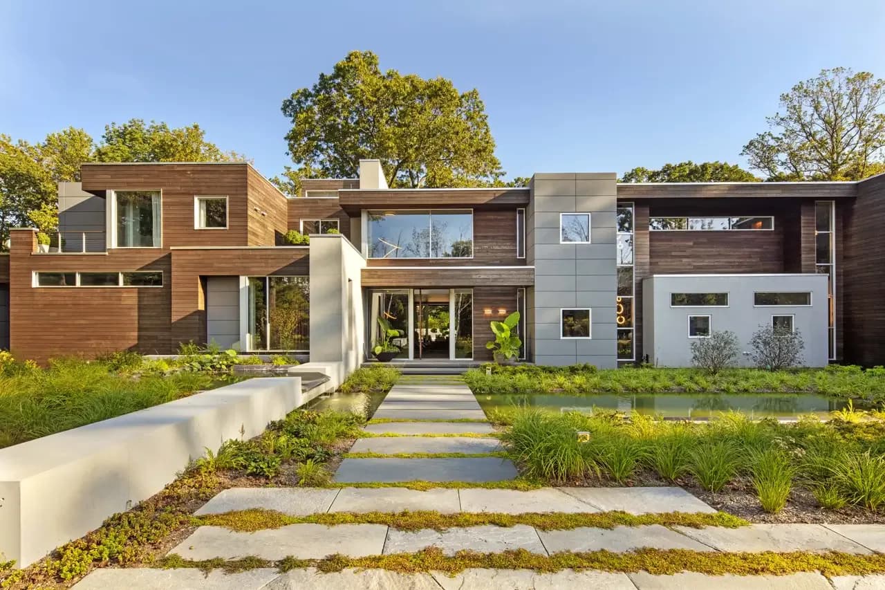 Contemporary residential architecture with mixed brick and metal cladding, glass entry, landscaped front garden with stone pathway by Sara Ledra.
