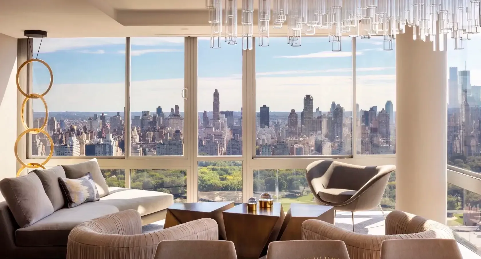 Luxurious high-rise residential living room with floor-to-ceiling windows overlooking Manhattan skyline, featuring neutral-toned seating, modern chandelier, and panoramic Central Park views by Sara Ledra.