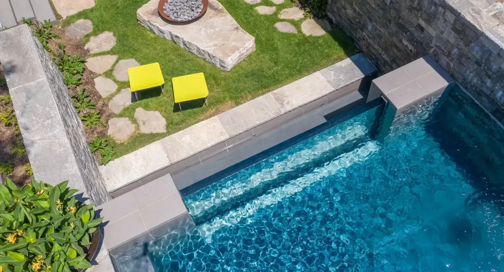 Contemporary poolside terrace with turquoise lap pool, concrete decking, yellow lounge chairs, and manicured lawn with stone pathways by Sara Ledra.