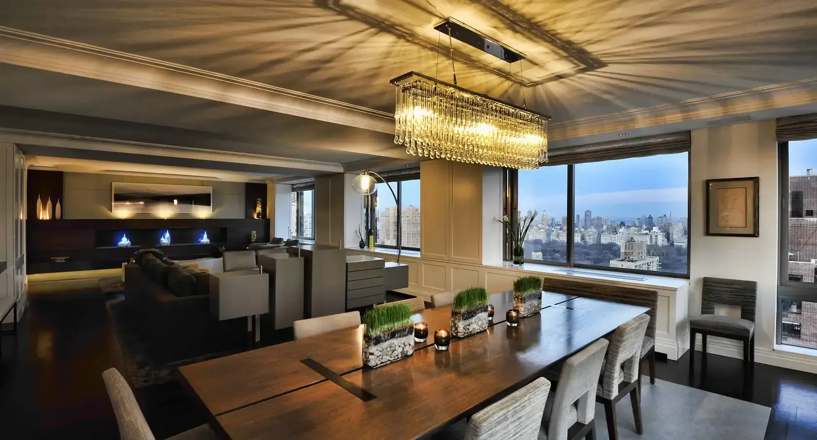 Modern luxury dining room with wood table, pendant lighting, and floor-to-ceiling windows overlooking cityscape by Sara Ledra.