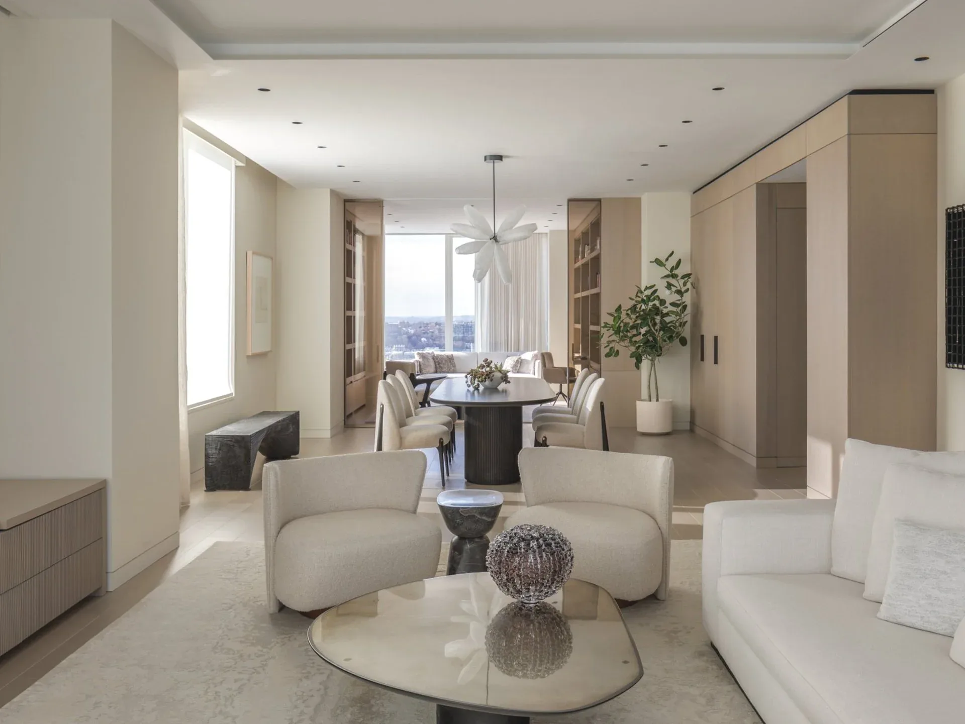 Luxurious modern apartment living room with curved cream furniture, marble round table, and floor-to-ceiling windows overlooking a city skyline by Sarah Witkin.