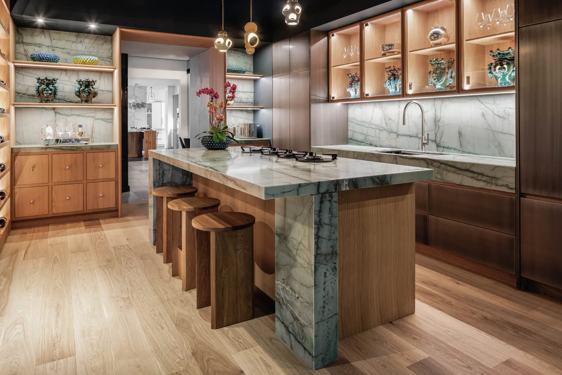 Modern kitchen with warm wood cabinetry, white marble countertops, and a waterfall island with wood and stone base by Sarah Witkin.