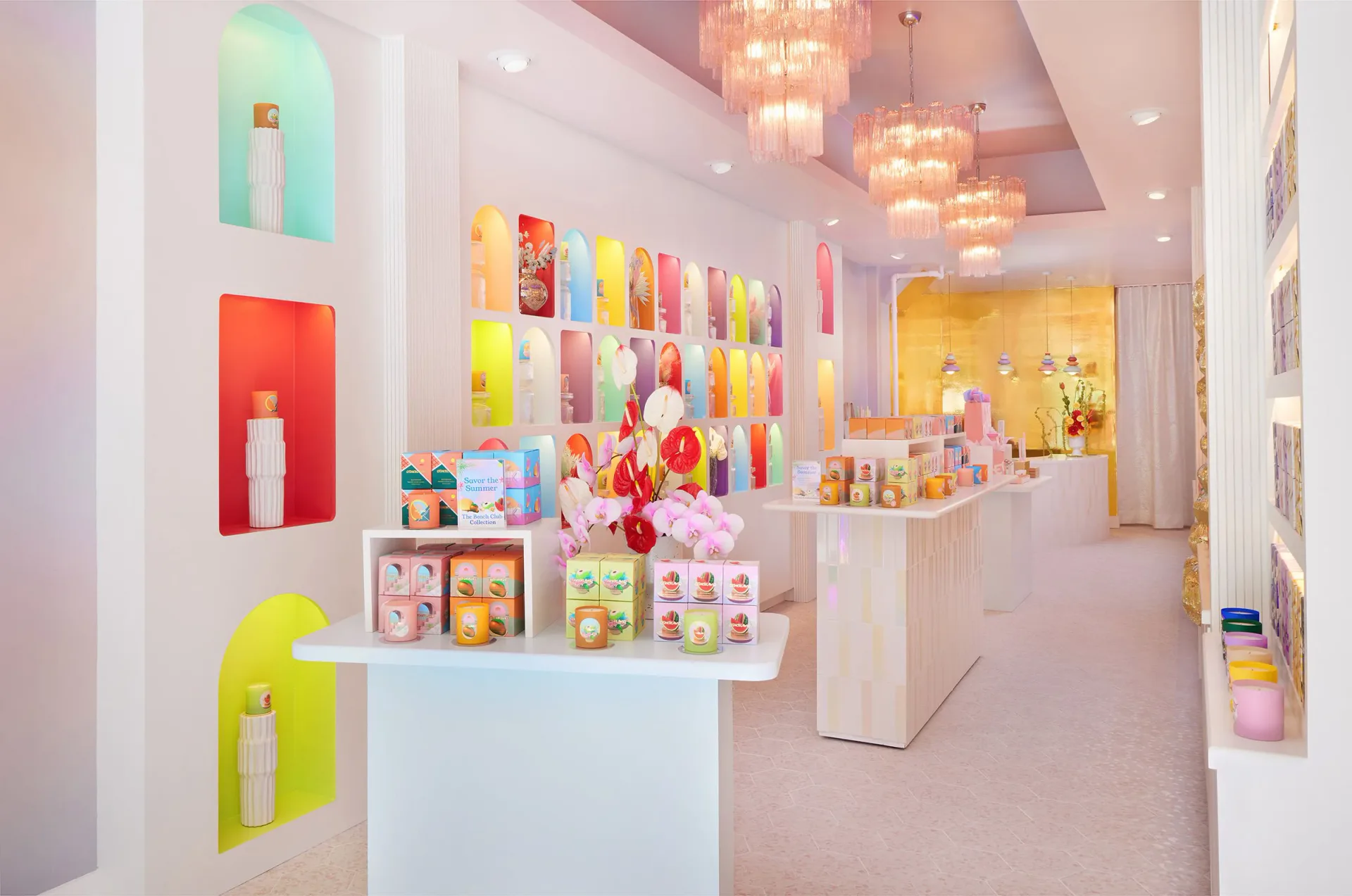 Bright retail interior with colorful product displays on white shelving and walls, featuring vibrant packaging and hanging pendant lights, designed by Sasha Bikoff.