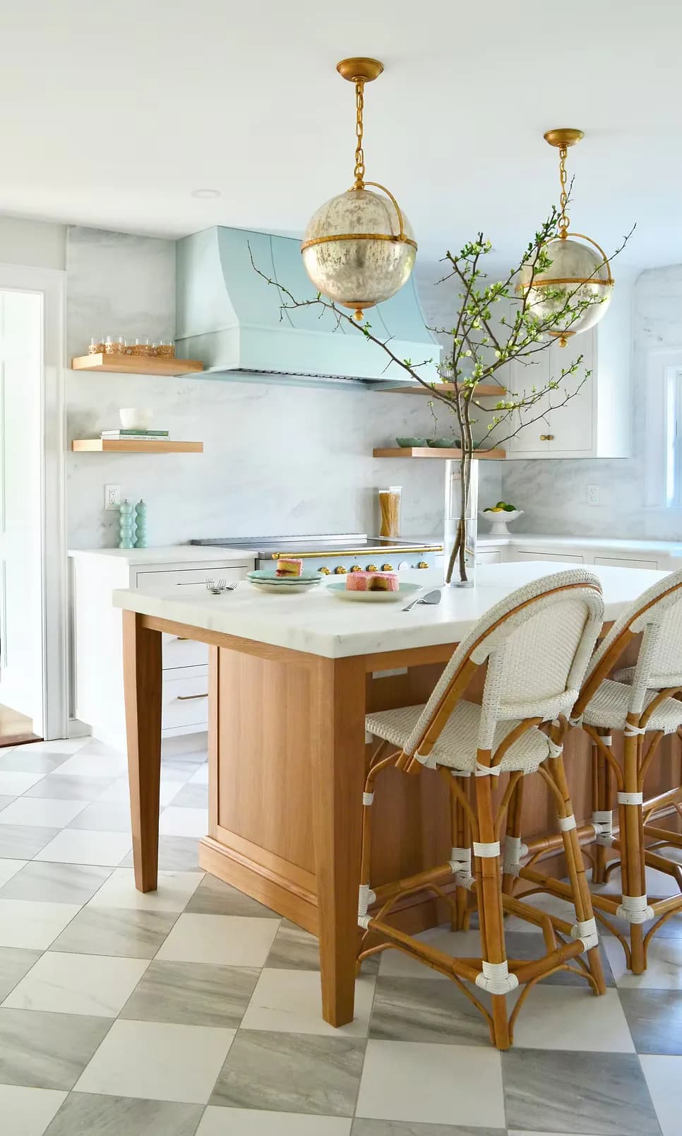A modern kitchen with a wood island, white marble countertop, brass pendant lights, and woven bar stools by Schuyler Johnson.