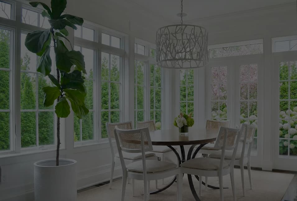 Bright, minimalist dining room with white furniture, extensive glazing, potted plant, and wire pendant light by Schuyler Johnson.
