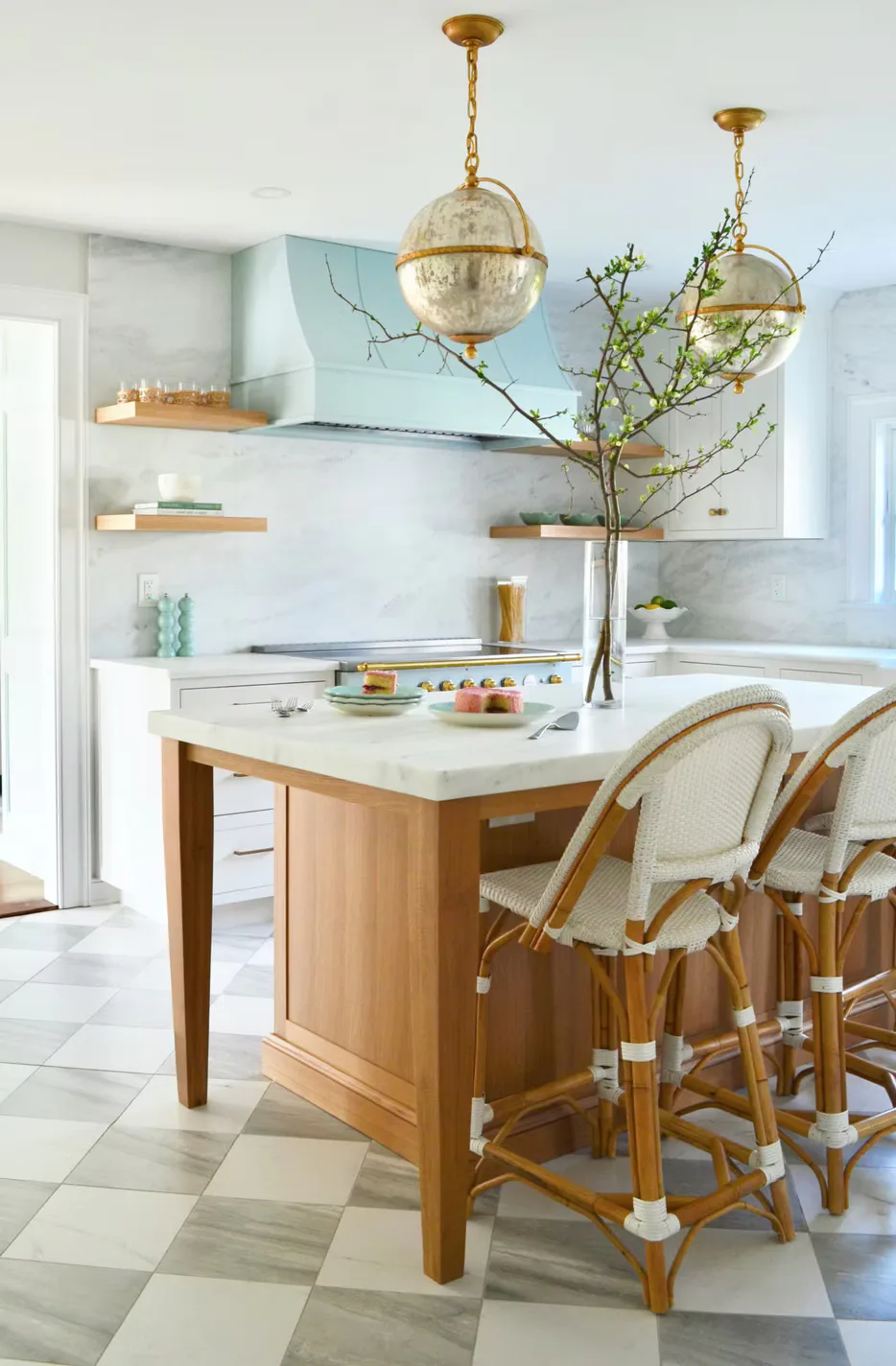 Modern kitchen with marble backsplash, wood island with white countertop, brass globe pendant lights, and woven bar stools by Schuyler Johnson.