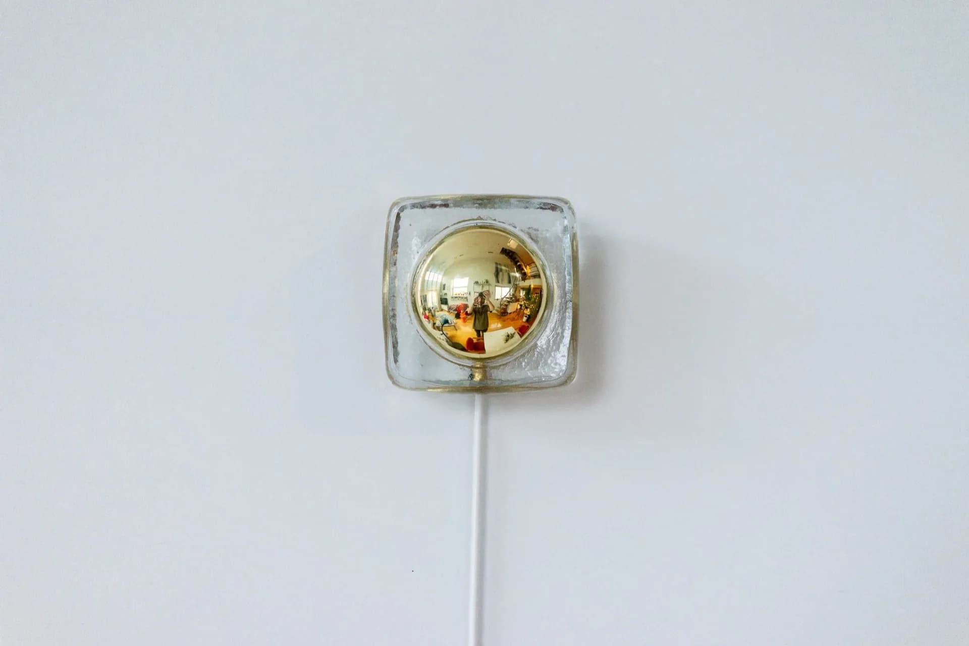Minimalist wall-mounted light fixture with golden spherical bulb encased in clear glass square housing and white cord by Sebastian Bidegain.