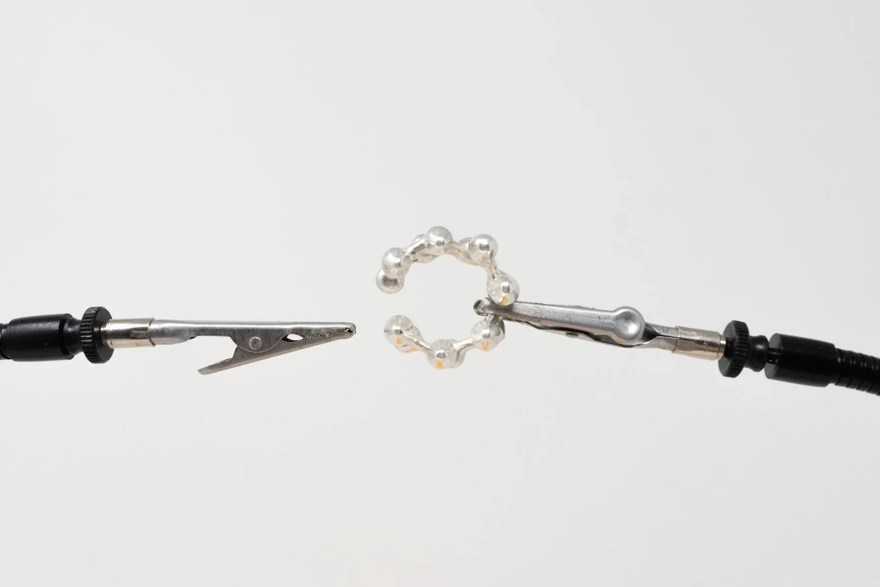 Delicate jewelry piece featuring black cord with metal implements and a central pearl beaded ring, handcrafted design by Sebastian Bidegain.