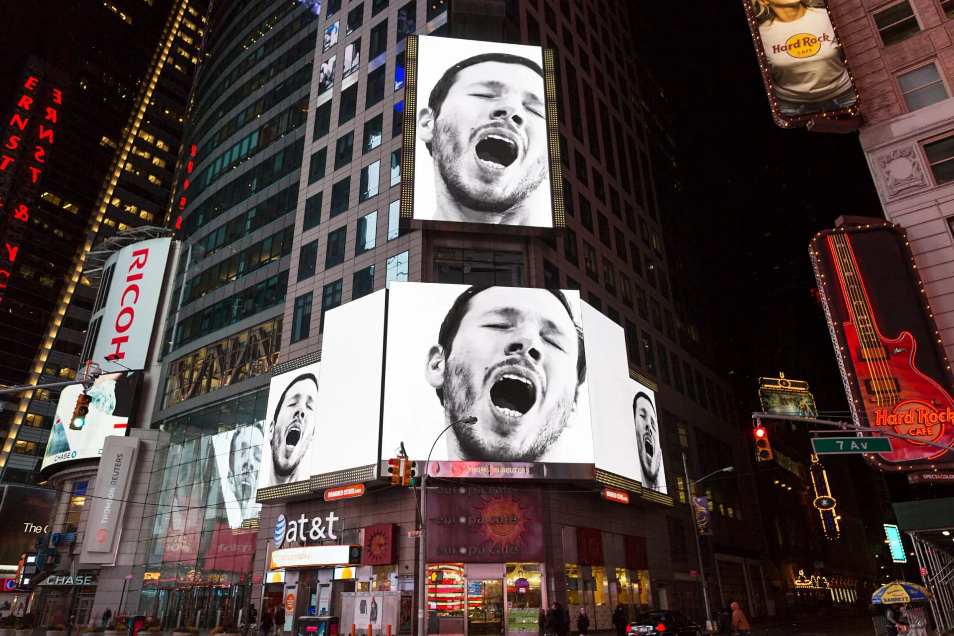 Times Square digital billboard installation displaying large-scale black and white portrait photography at night, surrounded by urban signage and lit buildings by Sebastian Errazuriz.