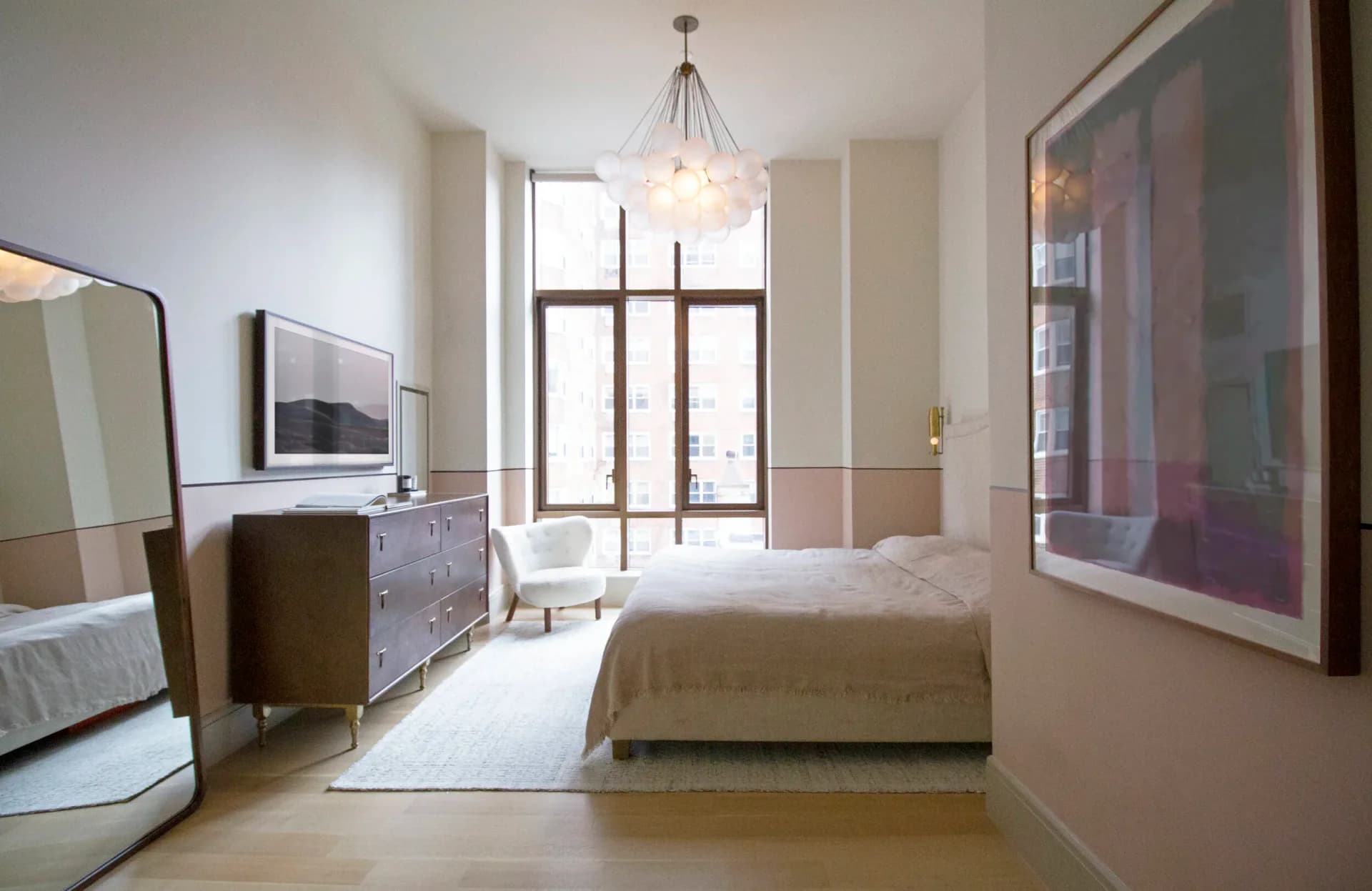 Modern bedroom with warm beige tones, featuring a platform bed, wooden dresser, pendant lighting, and floor-to-ceiling windows, designed by Sey Jeong.