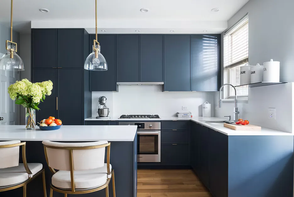 Modern kitchen with navy cabinetry, white countertops, pendant lighting, and dining area with mid-century chairs by Shai Arviv.