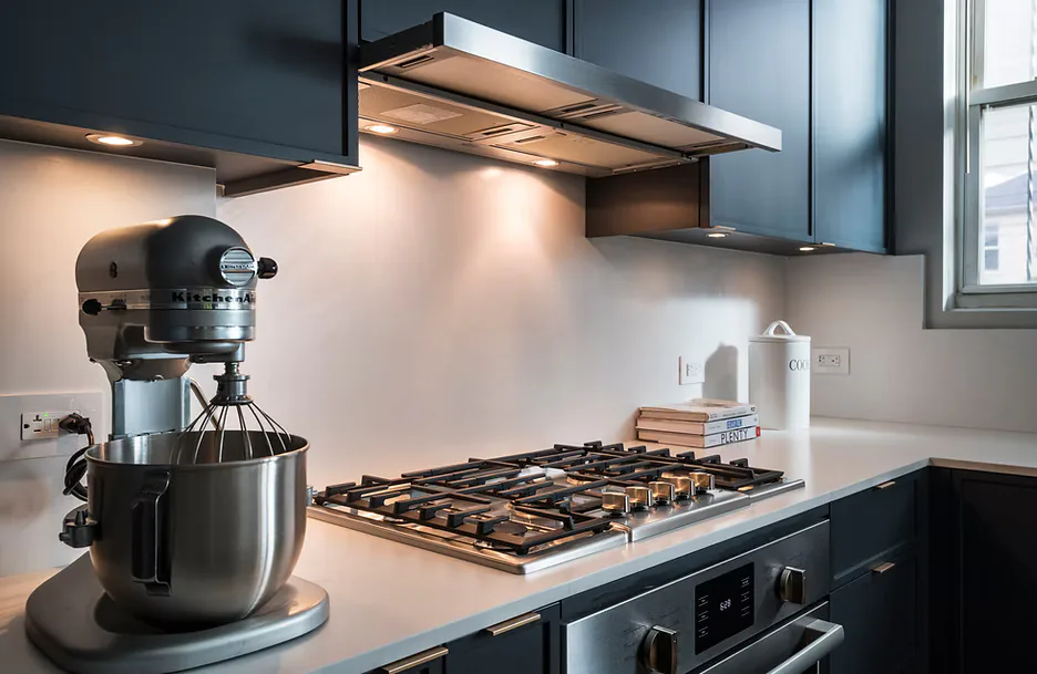 Modern kitchen with dark blue cabinetry, white backsplash, gas cooktop, and stainless steel appliances designed by Shai Arviv.