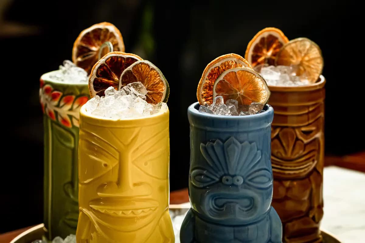 Four colorful tropical cocktails with embossed ceramic vessels, crushed ice, and dried citrus garnishes by Shaila Rizvi.