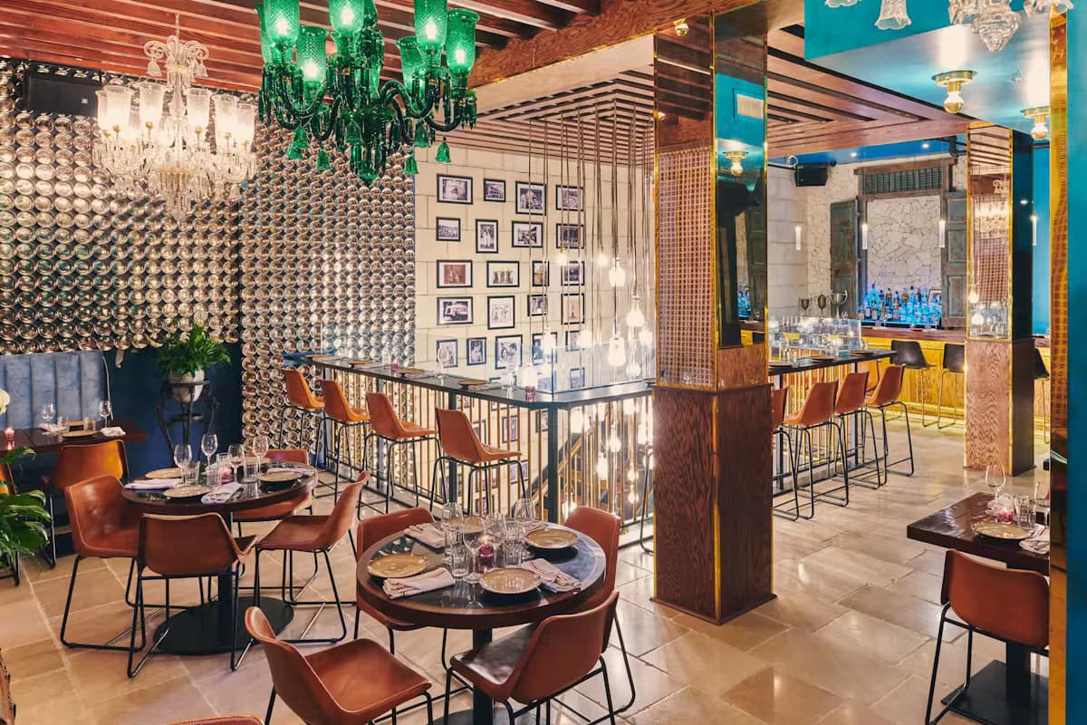 Contemporary restaurant interior featuring terracotta leather seating, geometric patterned walls, green pendant lighting, and circular dining tables by Shaila Rizvi.