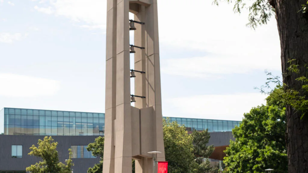 Modern architectural tower with vertical ribbed concrete facade and integrated lighting, adjacent to contemporary glass building framed by mature trees, by Shalin Dave.