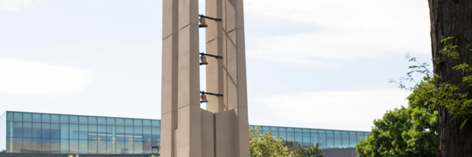 Modern concrete bell tower with vertical lighting elements flanked by contemporary glass buildings under cloudy sky, by Shalin Dave.
