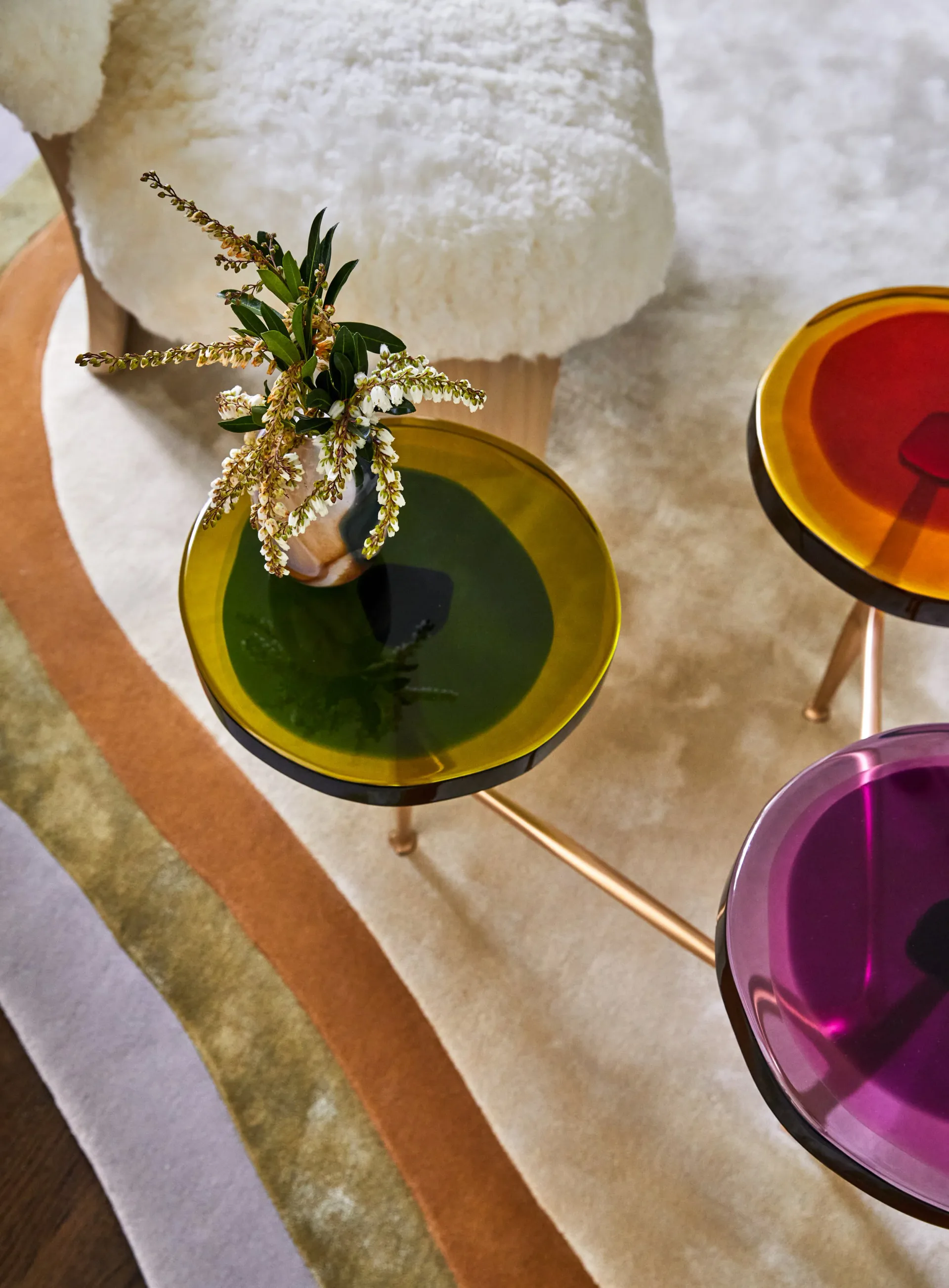 Styled flat lay featuring colorful cocktail glasses with green, amber, and purple liquids, fresh botanical garnish, and cream textile elements by Shana Shaiman.