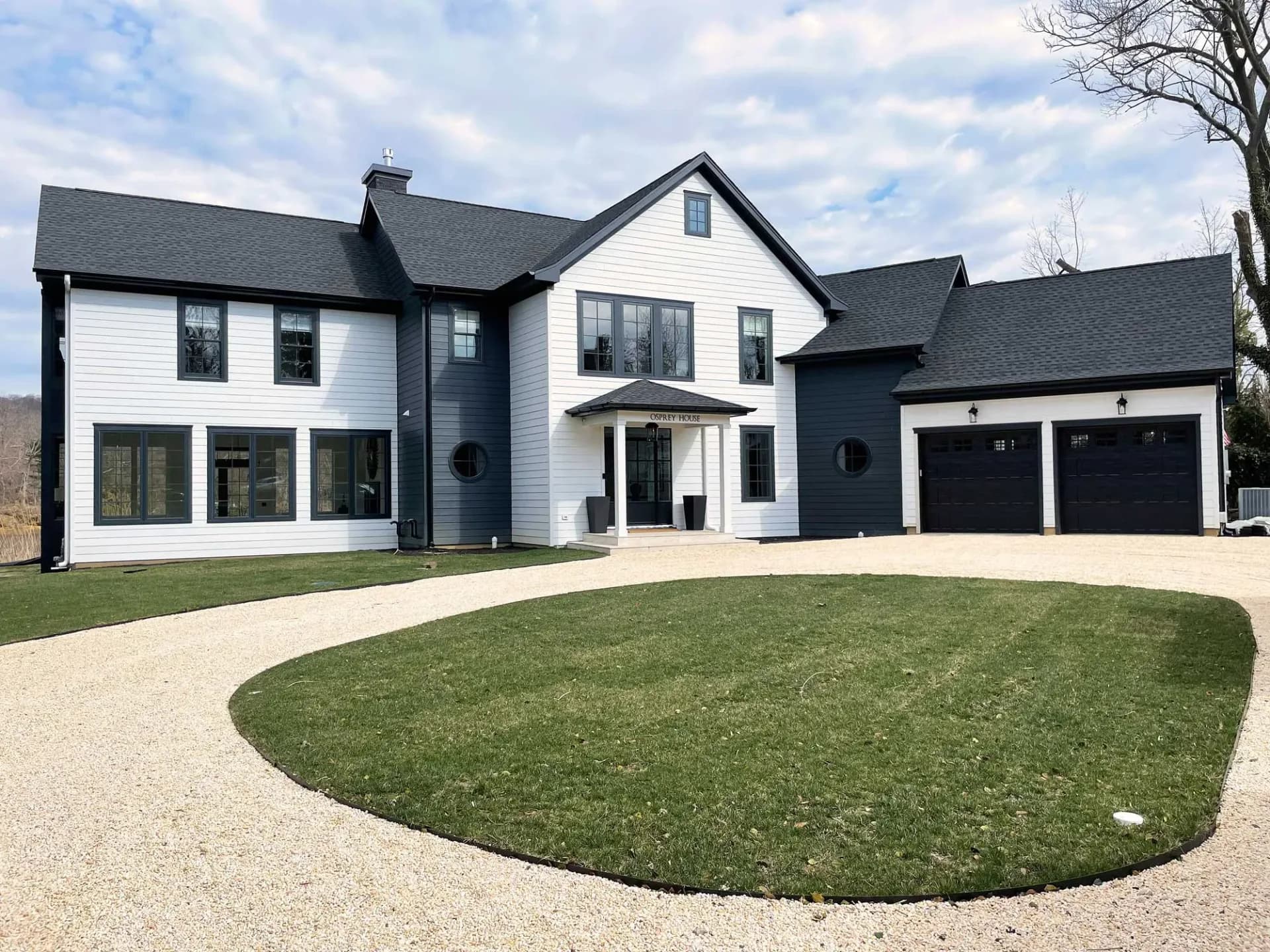 Modern two-story residential home featuring white and dark exterior with curved driveway, manicured lawn, and attached garage by Shayna Vrabel.