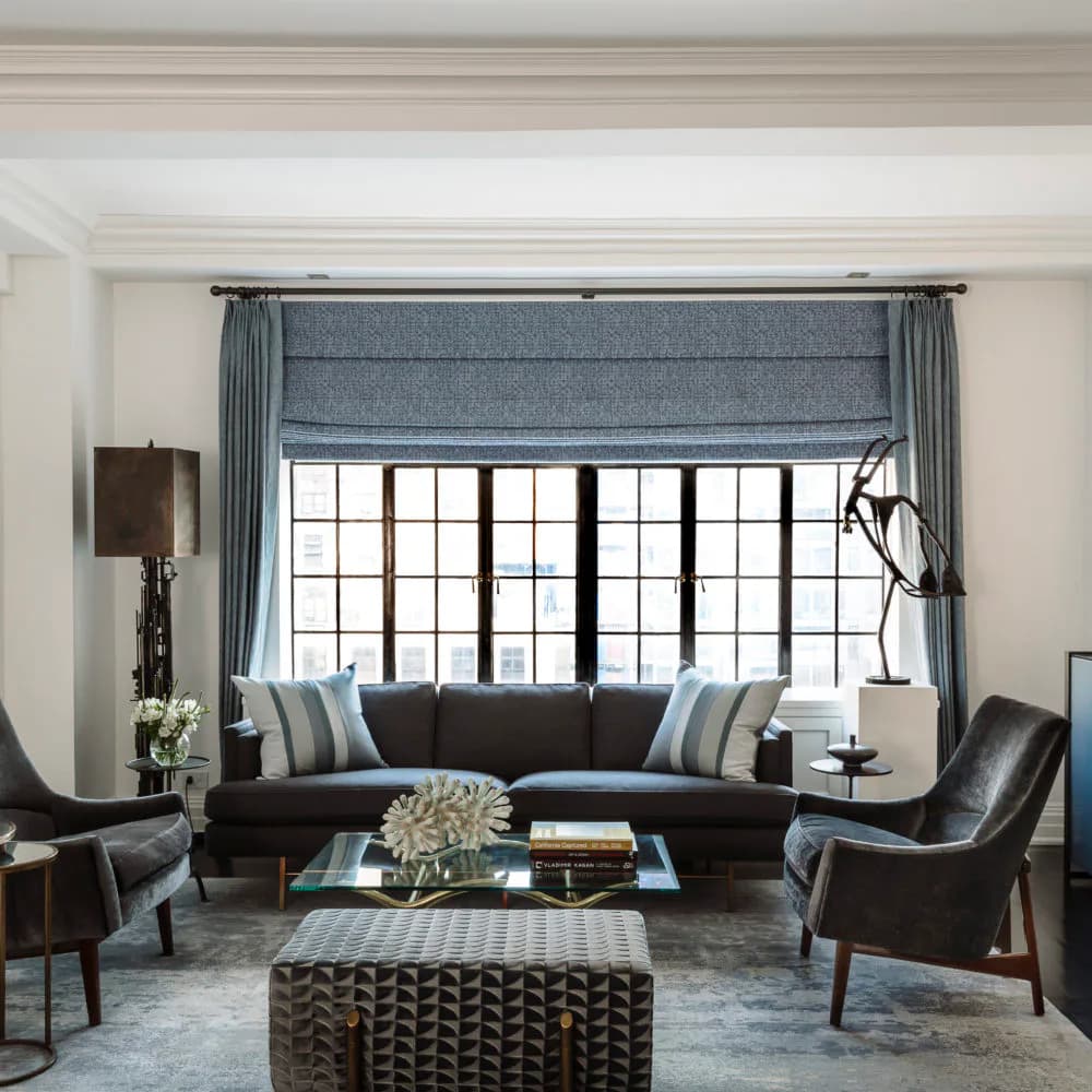 Contemporary living room with black curved sofa, blue-gray curtains, patterned ottoman, and leather accent chairs, designed by Sheila Bridges.