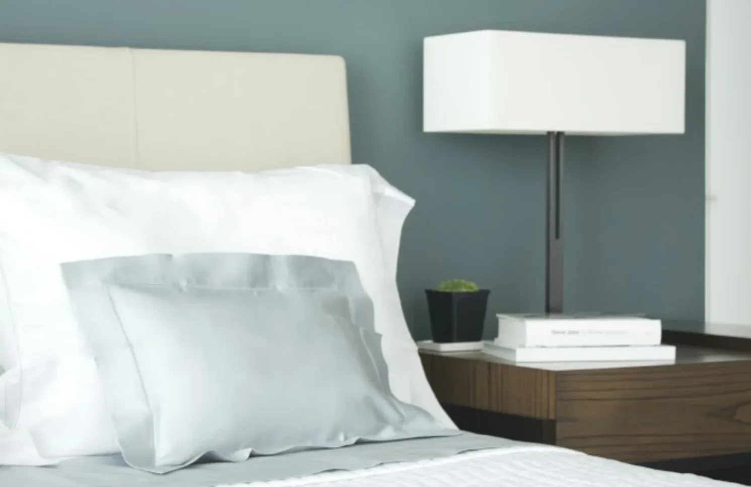 Modern bedroom with teal accent wall, white upholstered headboard, light blue pillow, dark wood nightstand with floor lamp, and white bedding by Sherry Brous.