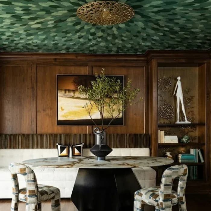 Dining room with round marble table, checkered chairs, wood paneling, green textured ceiling, and framed artwork by Simi Avidan.
