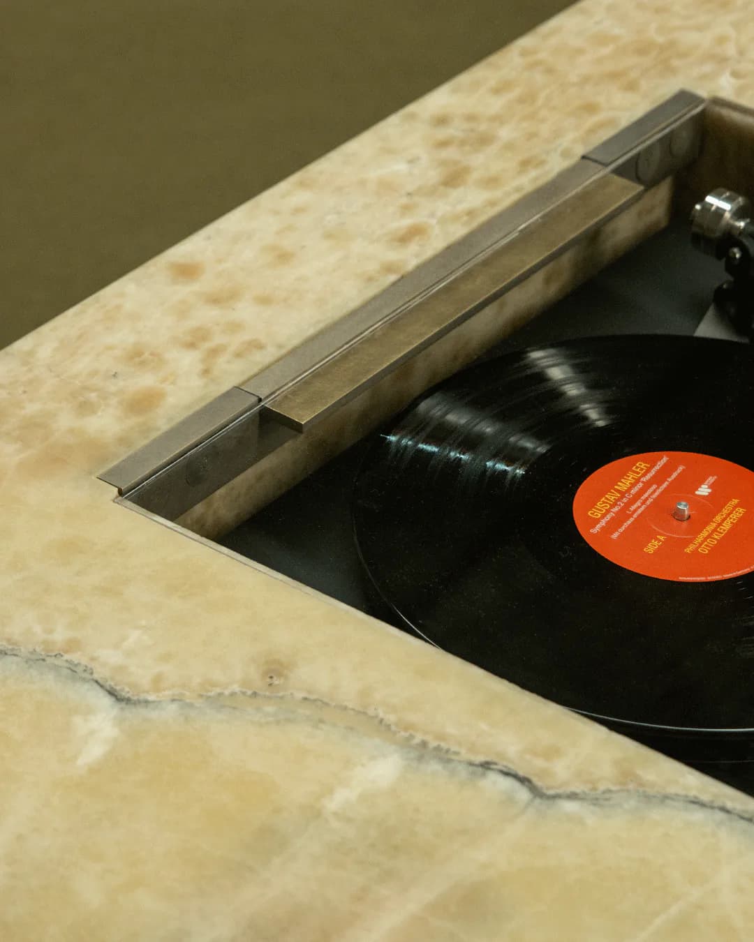 Built-in vinyl record storage with concrete surround and metal trim detail, featuring a black record with orange label by Simon Hamui.