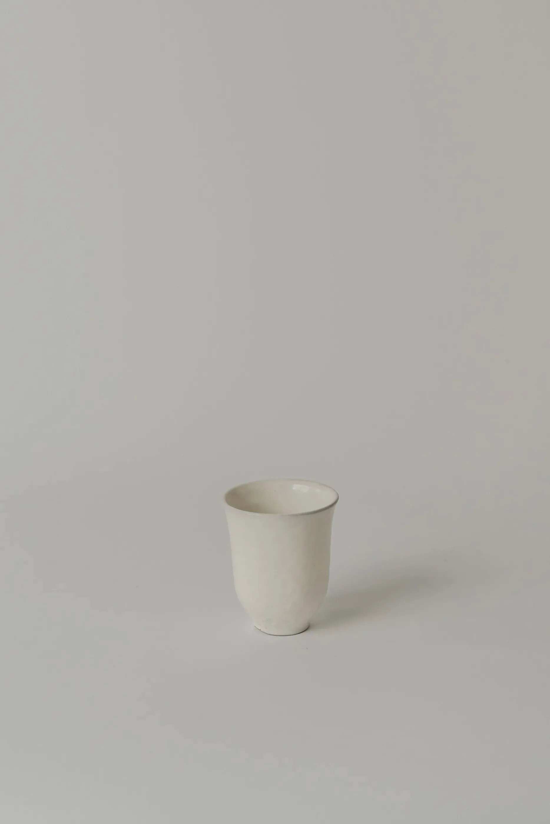 Minimalist ceramic vessel with soft cream glaze and subtle organic rim detail, photographed against neutral background by Simone Bodmer-Turner.