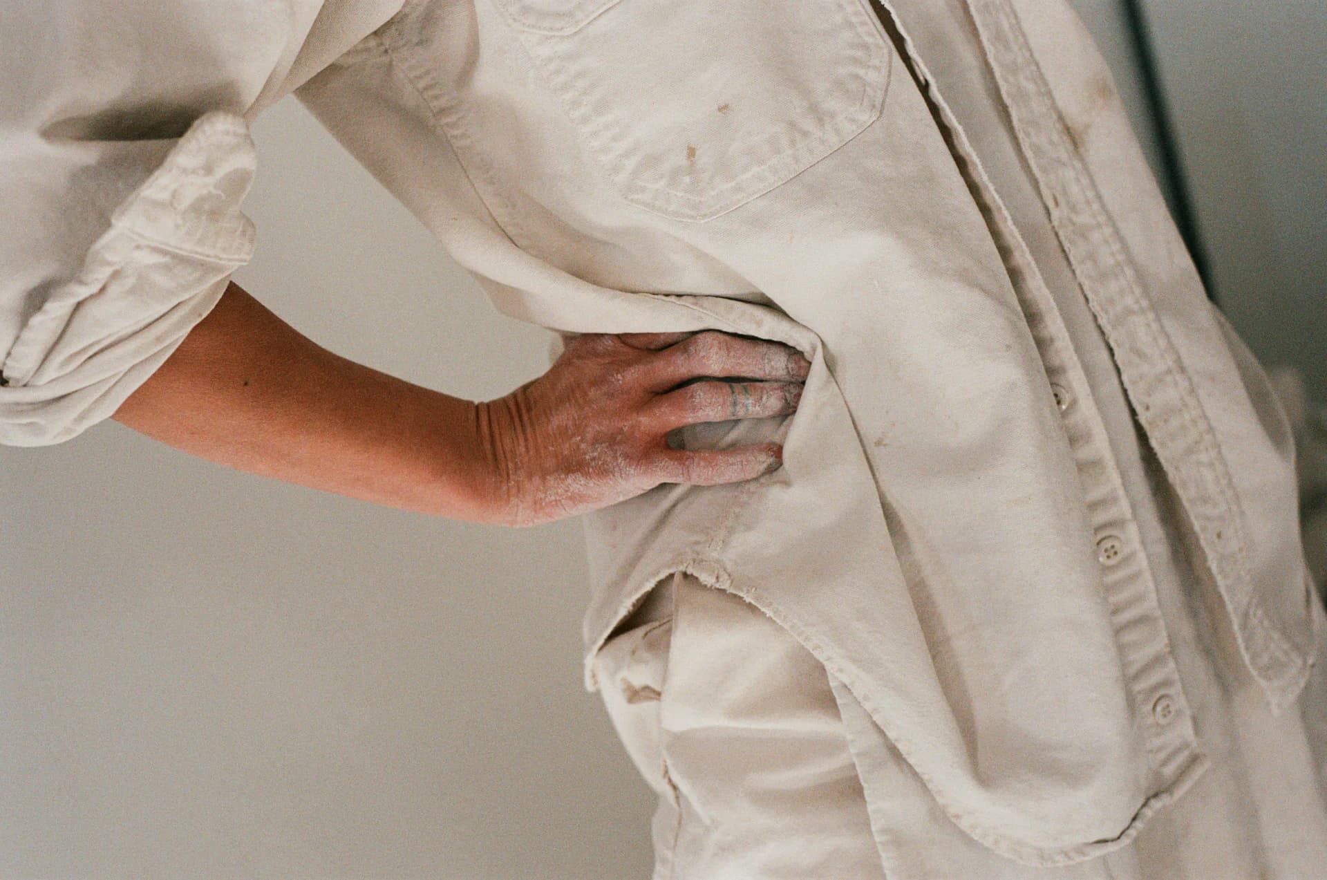 Close-up detail of cream-colored fabric garment with draped sleeves and textured weave, showcasing tailored construction by Simone Bodmer-Turner.