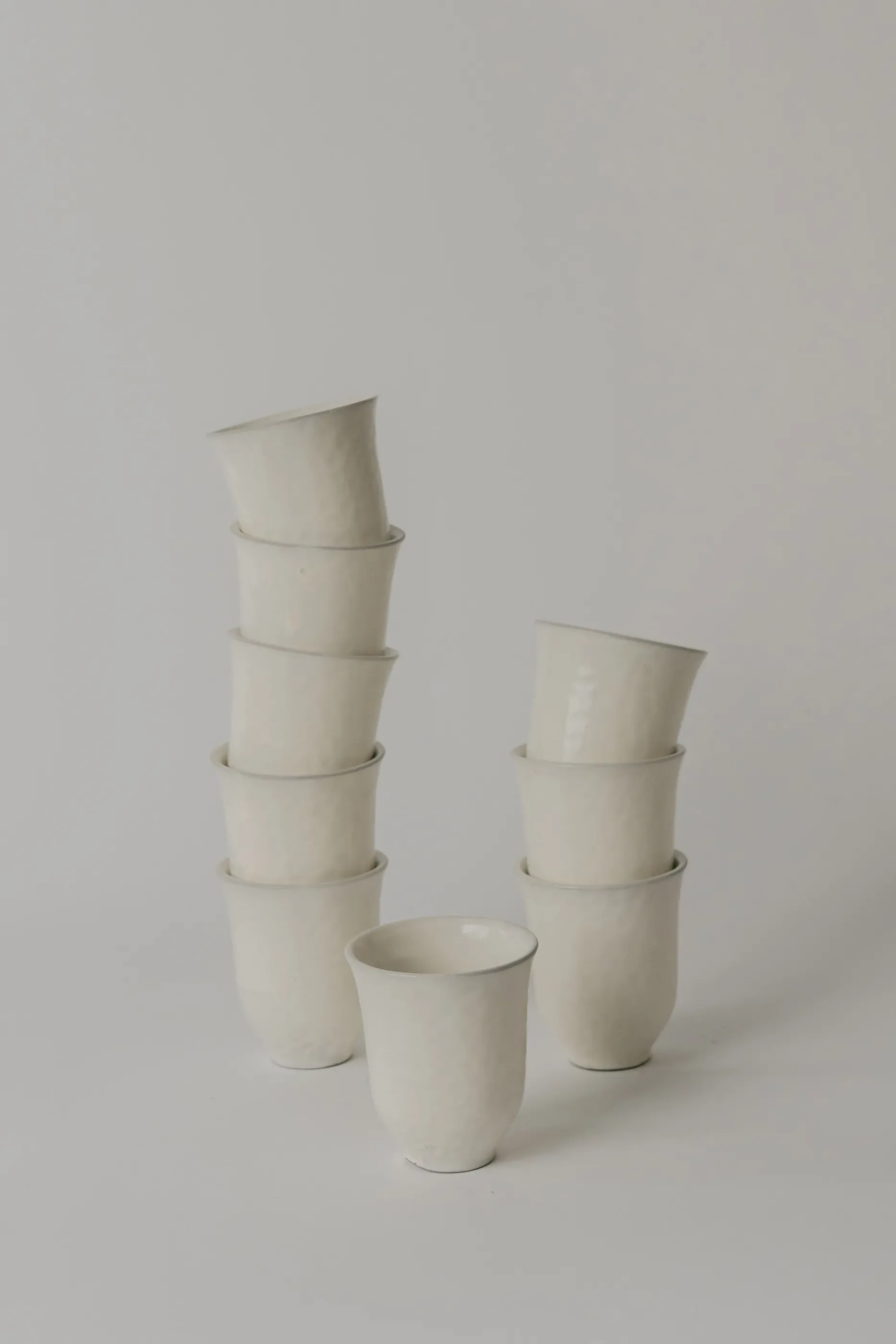 Stacked ceramic vessels in cream white, arranged in two towers with a single cup in front, showcasing functional pottery design by Simone Bodmer-Turner.
