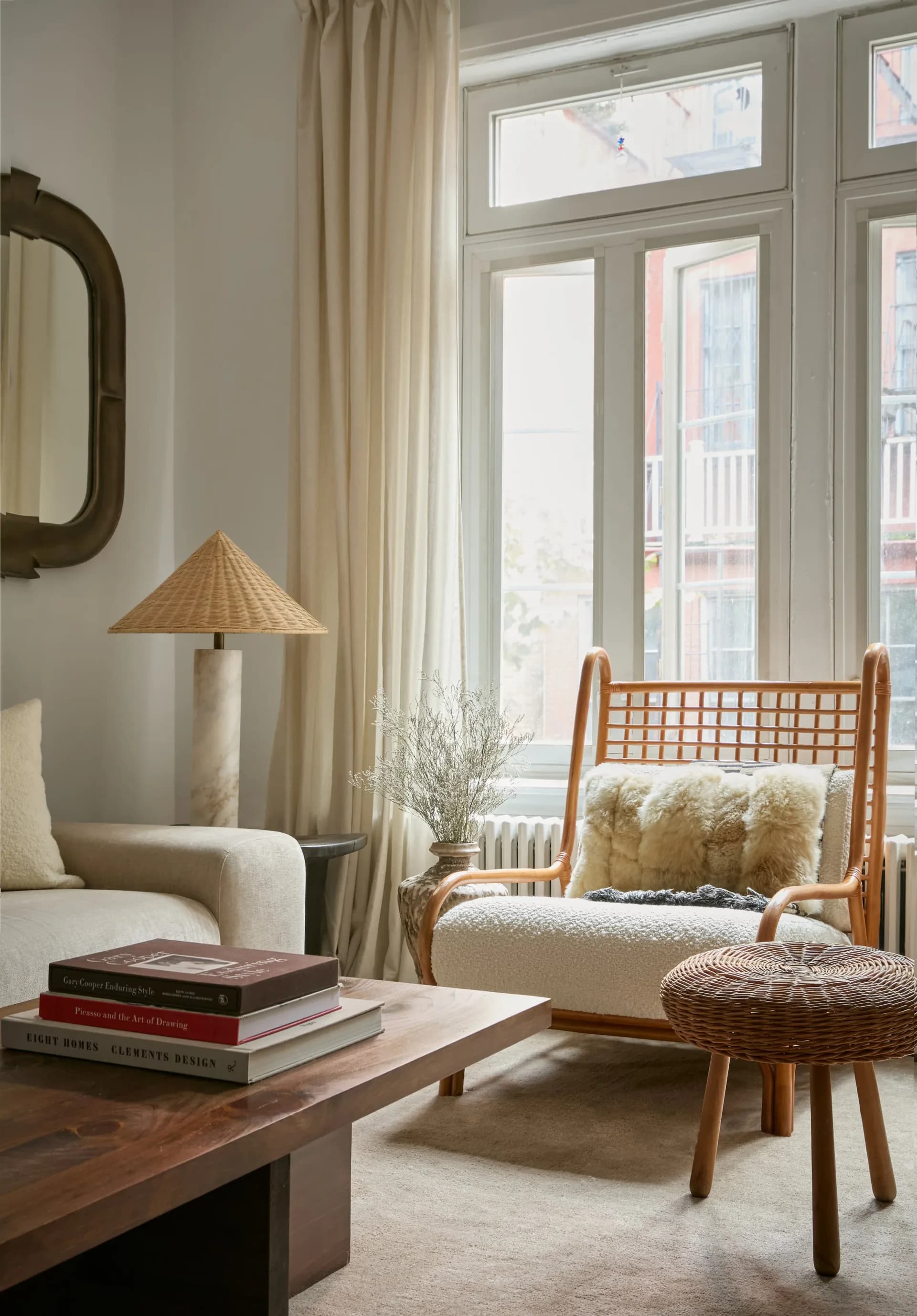 Bright living room with warm wood furniture, woven pendant lamp, cream upholstery, and large windows by Simone Lawton.