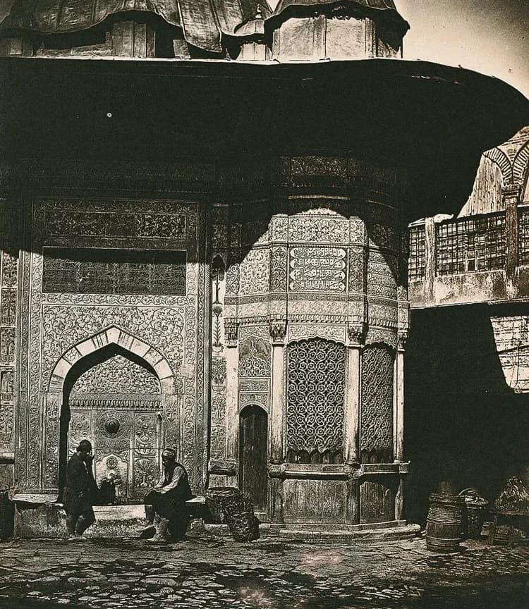 Ornate Islamic interior with arched doorways, geometric tilework, and intricate carved screens, photographed in sepia tones by Sisa Suriel.